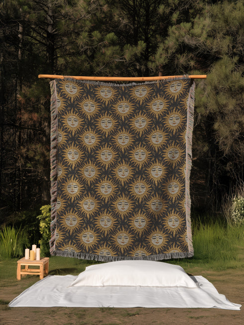 A woven cotton throw featuring a celestial sun face pattern in gold and black tones, framed by soft fringe.